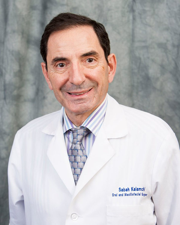 Headshot of Dr. Kalamchi with white coat and gray background.