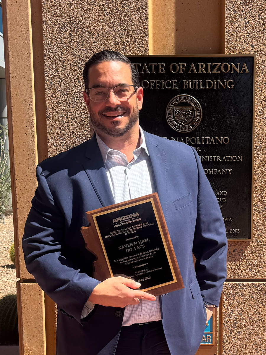 Dr. Kaveh Najafi in a blue suit holding his Arizona Trauma Medical Director of the Year plaque outside the State of Arizona office building.