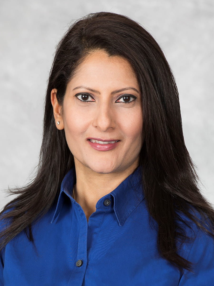 Professional headshot of Dr. Shalini Singh-Karnik wearing a blue button-down shirt against a light gray background.