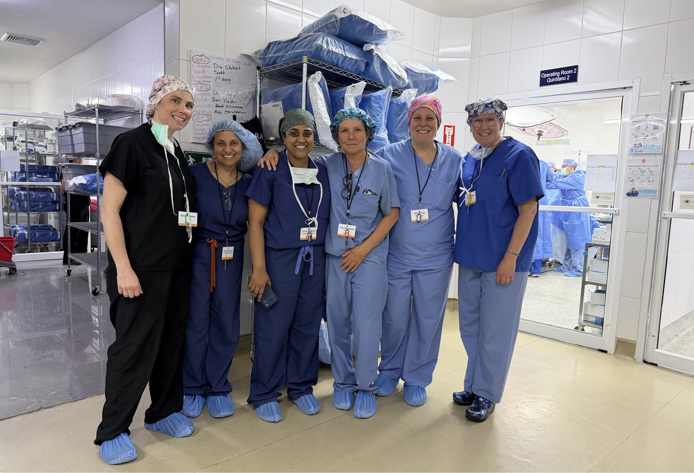 Dr. Shankar and five medical team members wearing scrubs and surgical caps pose together in a hospital hallway outside an operating room in Honduras.